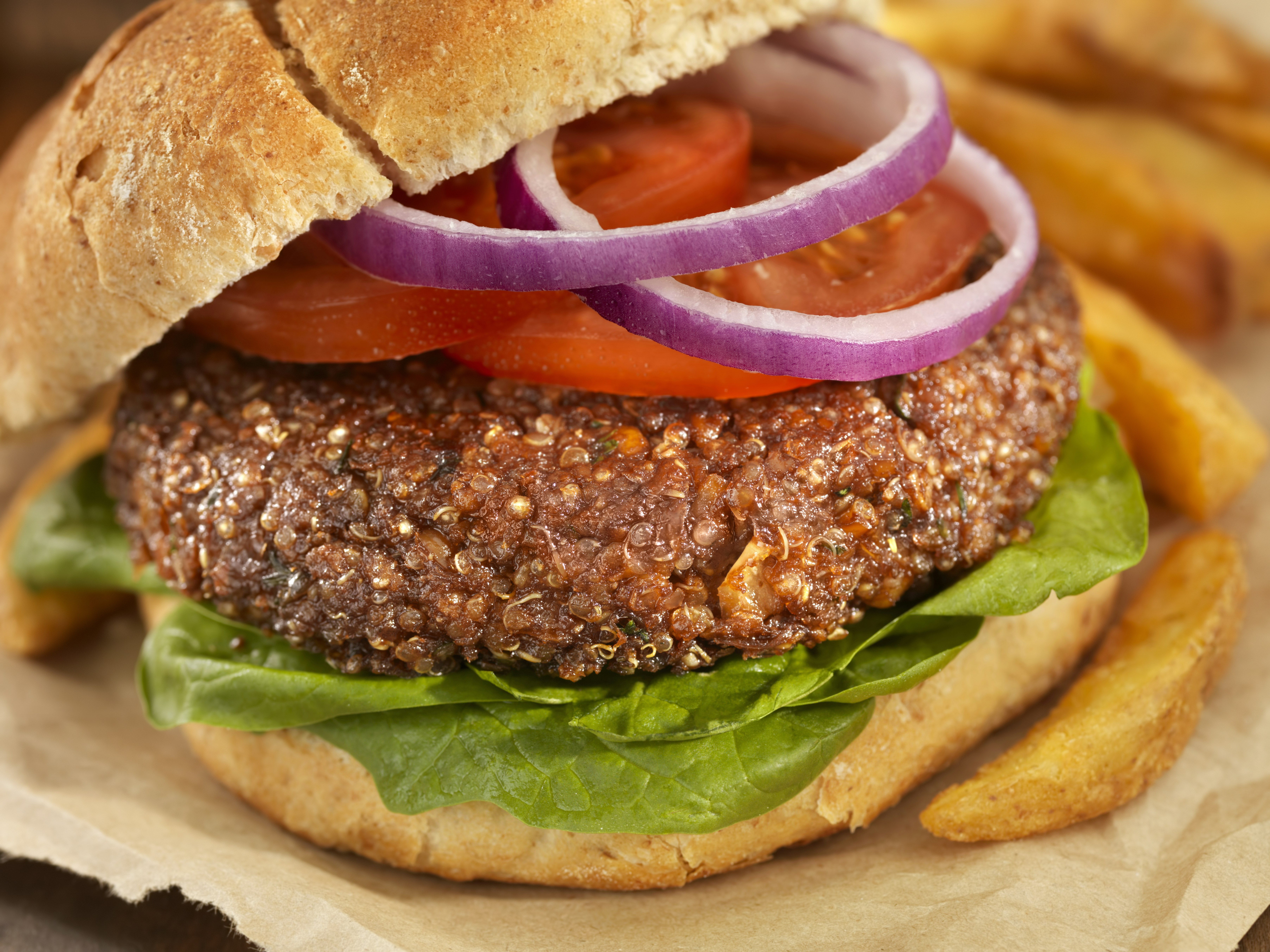 Closeup of a quinoa burger on a whole wheat bun with slices of tomato and onion on top.
